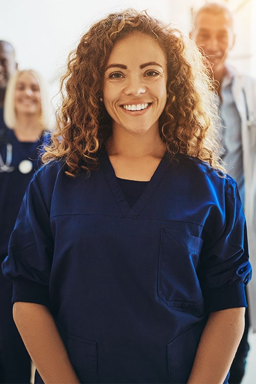 Empathetic healthcare professional smiling in medical scrubs with diverse team in background.