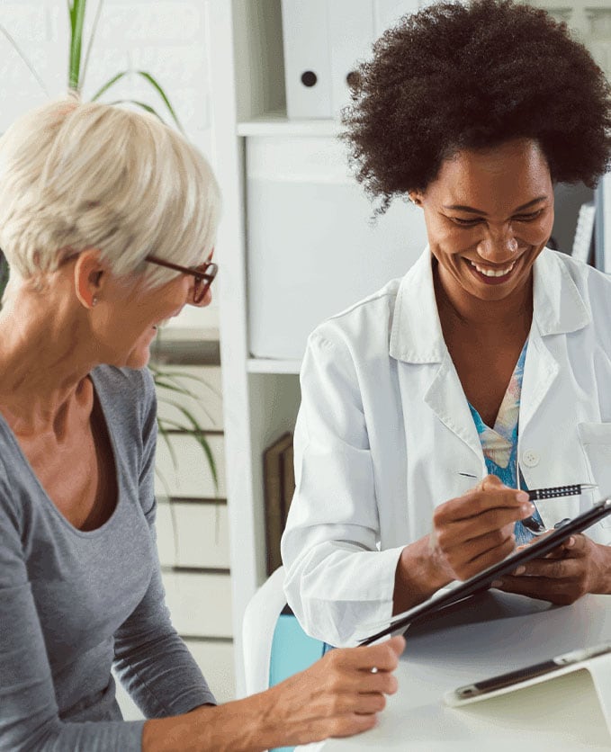 An African American female doctor reviews lab results with a white female patient in a grey shirt